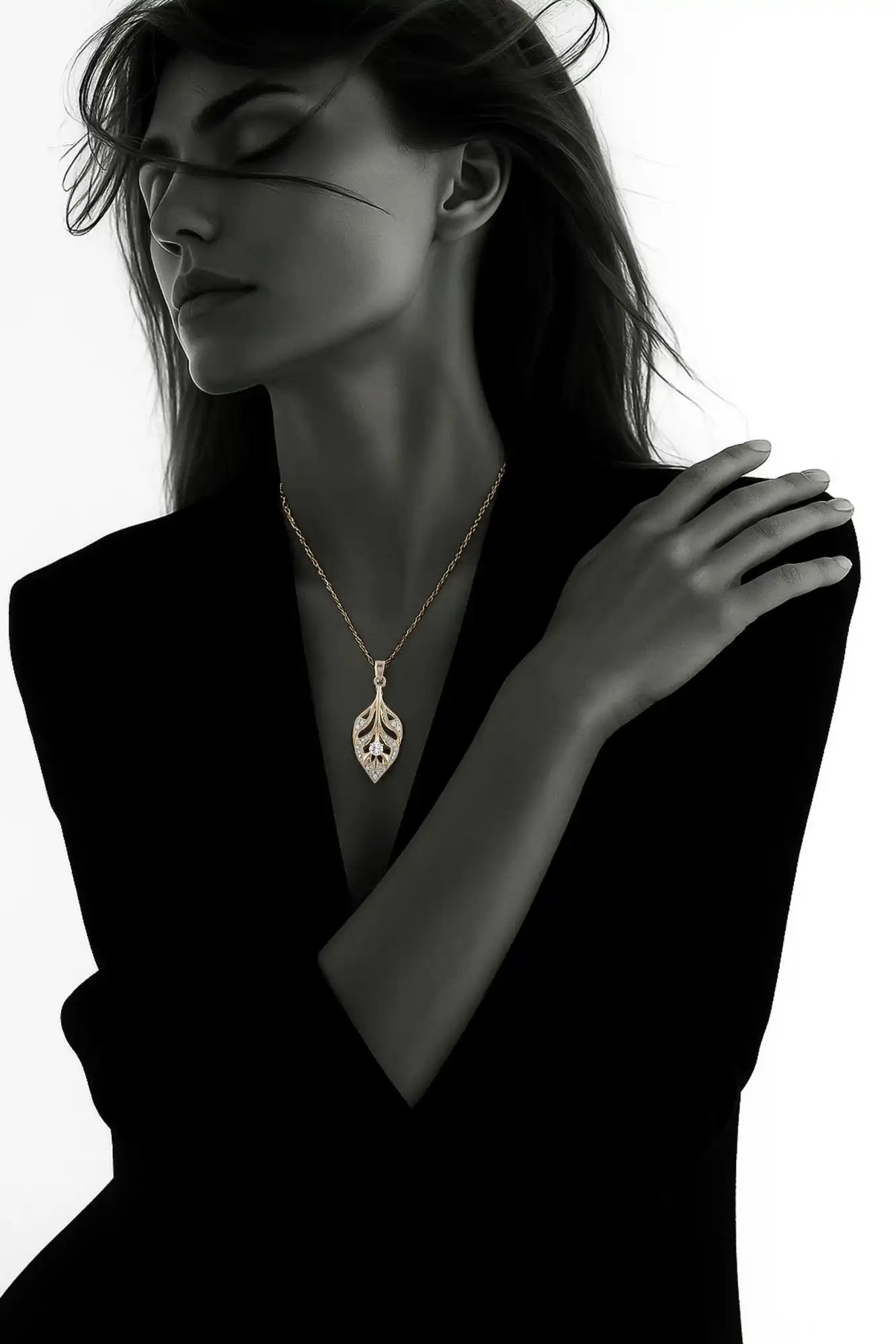 Un pendentif en forme de feuille d'or avec des détails complexes, peut-être ornée de petits diamants ou pierres précieuses, suspendu à une chaîne délicate.